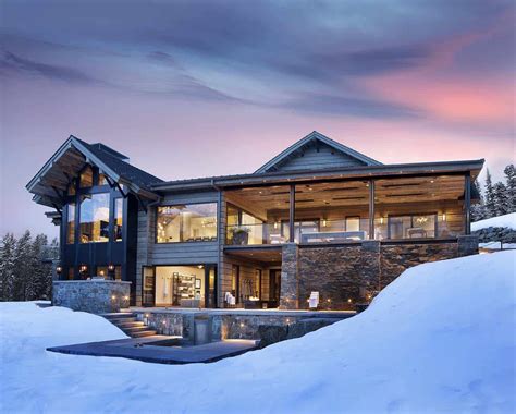A Large House Sitting On Top Of A Snow Covered Hill Next To A Lake At Dusk