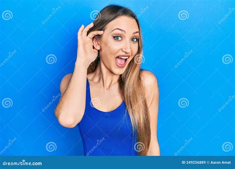 Young Blonde Girl Doing Listen Gesture With Hand On Ear Celebrating