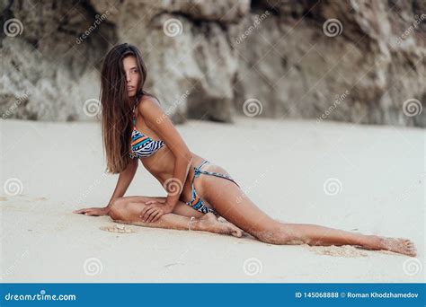 Slender Tanned Woman In Colored Swimsuit Posing On Beach With White