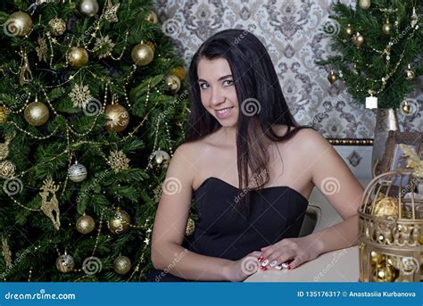 Beautiful Girl In A Black Dress On The Background Of The Christmas Tree