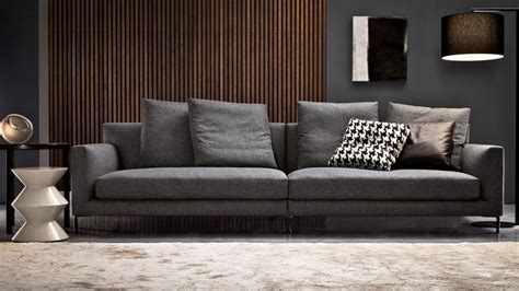 A Living Room With A Gray Couch And Wooden Wall Behind The Couch Is A Lamp