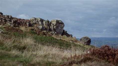 Some Very Big Rocks On The Side Of A Hill With Grass And Bushes Around Them