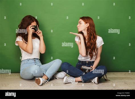 photo of two redhead girls 20s sitting on floor with legs crossed and playing in paparazzi with