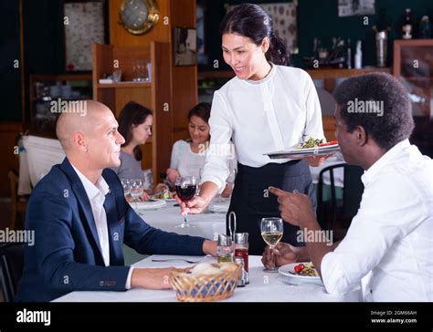 Female Waitress Serving Order From Male Customers In Cafe Stock Photo
