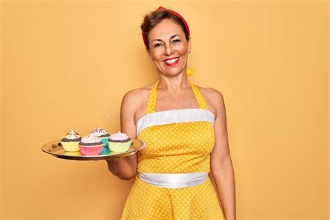 middle age senior pin up woman wearing 50s style retro dress holding tray with cupcakes with a