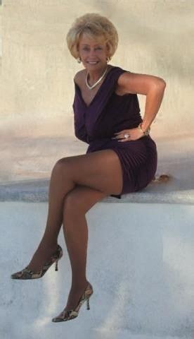 A Woman Sitting On Top Of A White Wall Wearing High Heeled Shoes And A Purple Dress