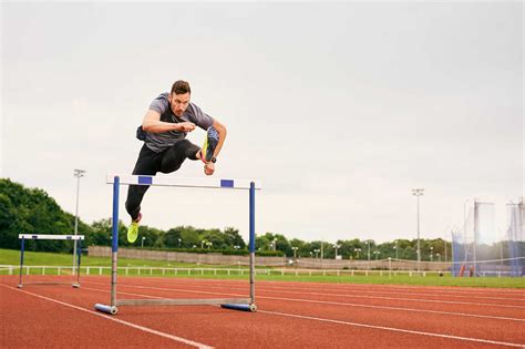 Athlete Jumping Over Hurdle On Running Track Stock Photo