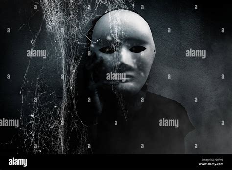 Mysterious woman in black wearing white mask hidden behind spider web