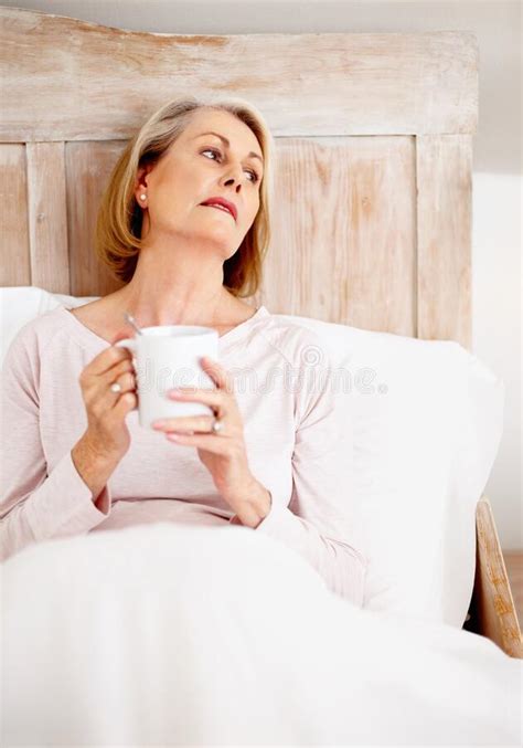 relaxed mature woman holding coffee mug in bed portrait of a relaxed mature woman holding