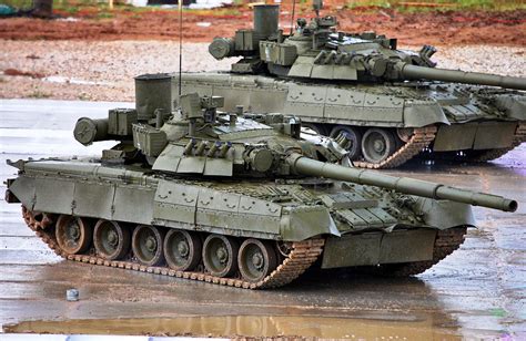 Two Army Tanks Sitting On Top Of A Wet Ground Next To Each Other In The