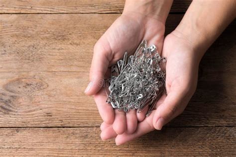 Woman Holding Pile Of Safety Pins At Wooden Table Top View Space For