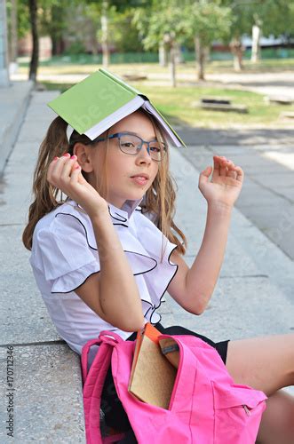 Cute Schoolgirl Of Primary School In Glasses Hides Under The Book Book