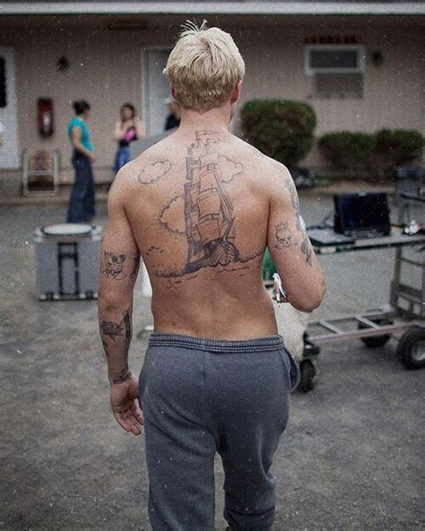 A Man With Tattoos On His Back Walking In Front Of A House