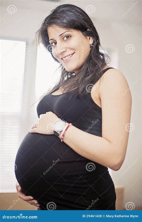 A Pregnant Indian Woman Smiling At The Camera And Standing Against A Black Background Stock