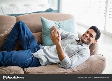Man Lying On Sofa And Using Mobile Phone In Living Room At Home Stock Photo By Wavebreakmedia