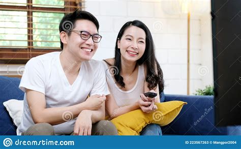 Happy Asian Couple Watching Television Show While Sitting On Safa At Home Living Room Stock