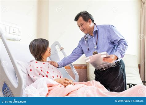 asian doctor reassuring female patient sitting on hospital bed during consultation stock image
