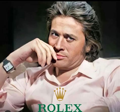 A Man Sitting Down With His Hand On His Chin And The Rolex Logo Behind Him