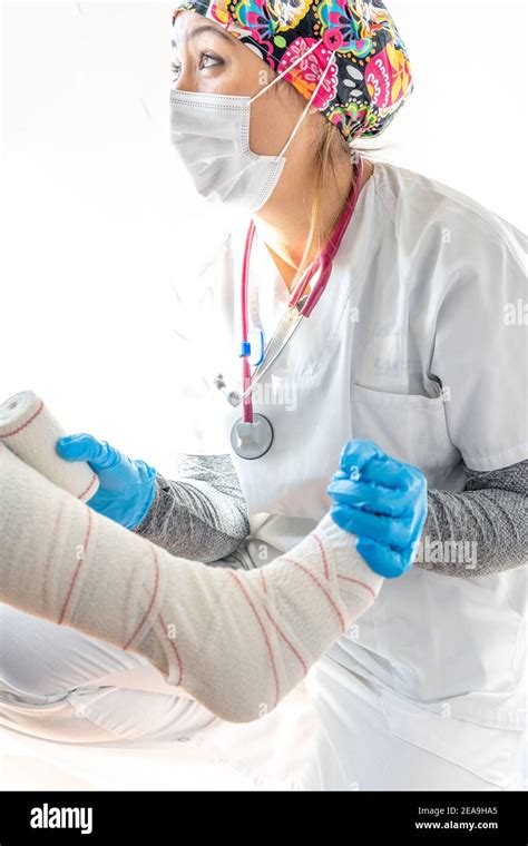 Crop Medic In Latex Gloves Wrapping Leg Of Unrecognizable Senior