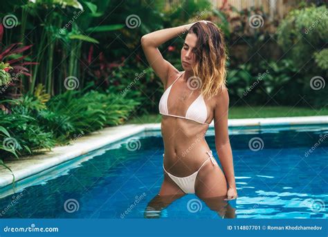 sexy mädchen steht in einem swimmingpool mit blauem wasser und in den tropischen bäumen auf