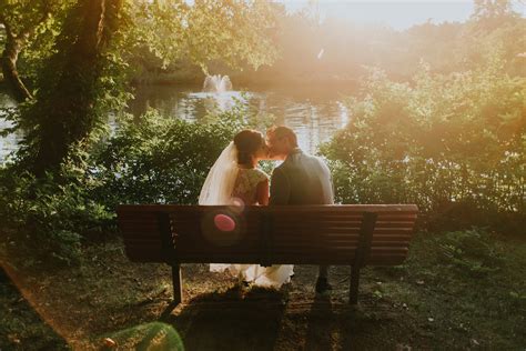 romantic sunlight over a just married couple kissing on a park bench at a lake bench at the