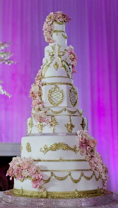 a three tiered wedding cake with pink flowers on the top and gold trimmings