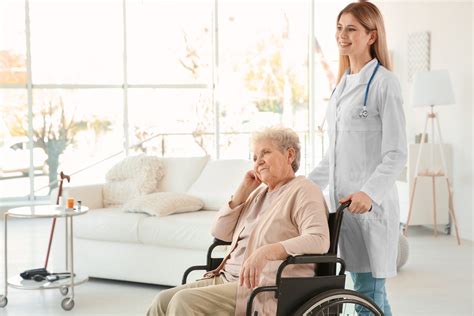 Young Nurse And Disabled Elderly Woman In Wheelchair At Home Cna