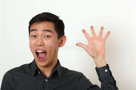 Smiling Young Asian Man Waving His Palm And Looking At Camera Stock