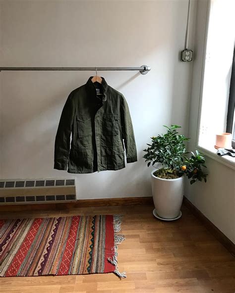A Green Jacket Hanging On A Clothes Rack Next To A Potted Plant And Rug