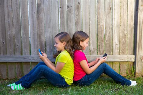 Twin Sister Girls Playing Tablet Pc Sitting On Backyard Lawn Stock