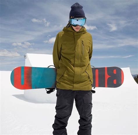 A Man Standing In The Snow With His Snowboard On His Back And Goggles On
