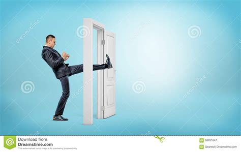 A Businessman In Side View Kicks A Small White Door Open With His Leg