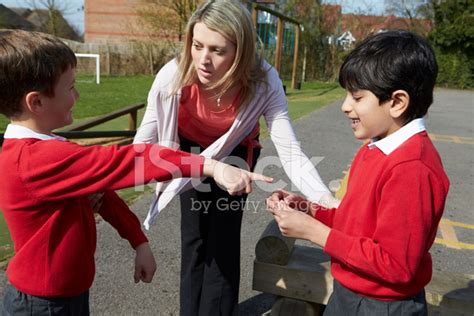 Teacher Stopping Two Boys Fighting In Playground Stock Photos