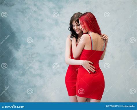 a close up portrait of two tenderly embracing women dressed in identical red dresses lesbian