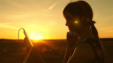 happy girl listening to music on smartphone in rays of a beautiful spring sunset slow motion