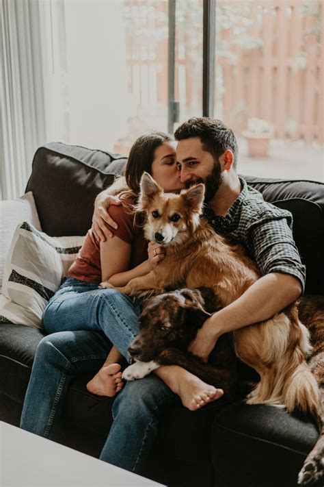 A Man And Woman Sitting On A Couch Cuddling With Two Dogs In Their Lap