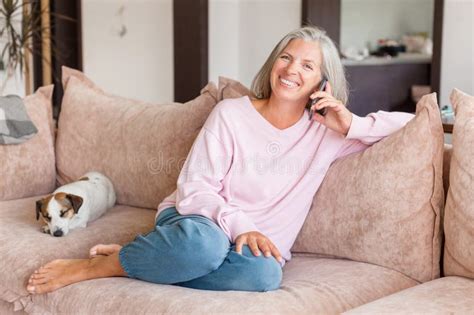 Pleased Middle Aged White Woman Talking On Mobile Phone On Couch Stock