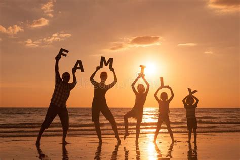 Família Feliz Que Está Na Praia No Tempo Do Por Do Sol Imagem De Stock