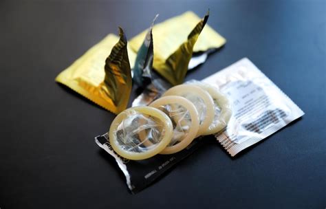Hiv와 안전한 섹스 포장지를 배경으로 콘돔을 들고 있는 손 안전한 섹스와 보호 촉진 프리미엄 사진