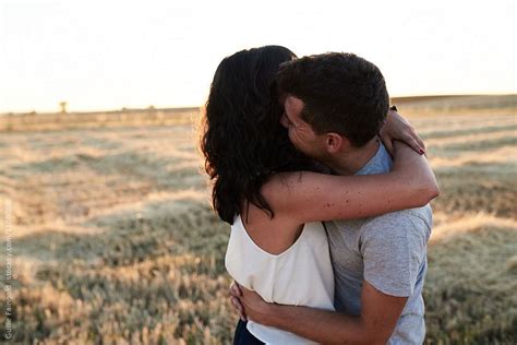 A Man And Woman Embracing Each Other In The Middle Of An Open Field At Sunset
