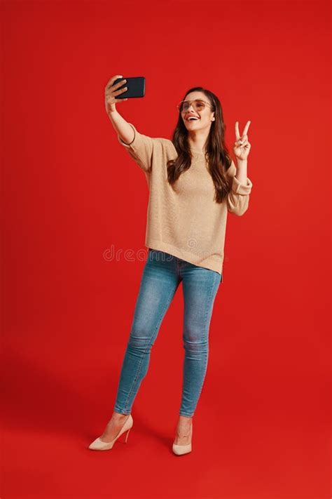 Full Length Of Playful Young Woman Taking Selfie While Standing Against Yellow Background Stock