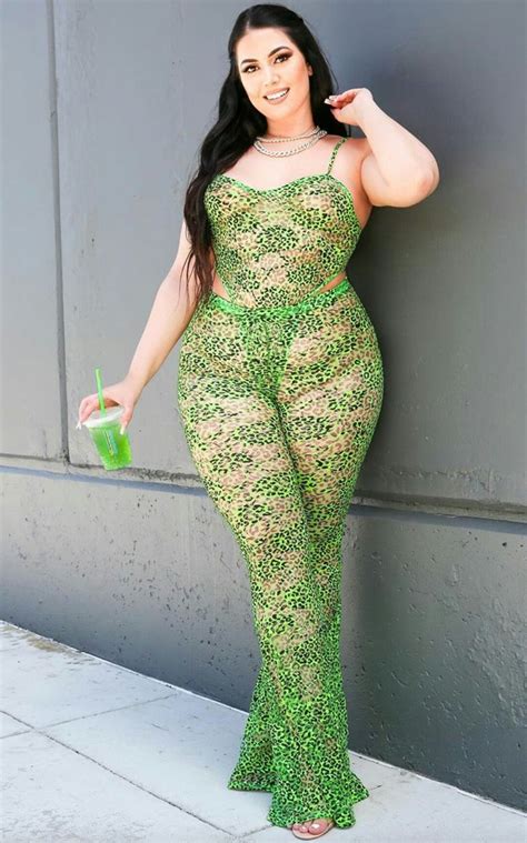 A Woman In Green And Gold Lace Jumpsuits Leaning Against A Wall With Her Hand On Her Hip