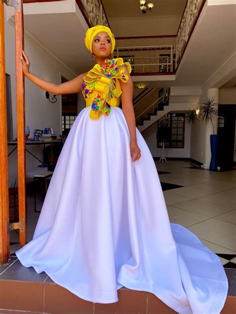 A Woman Wearing A White Dress And Yellow Head Scarf Standing In Front Of A Doorway