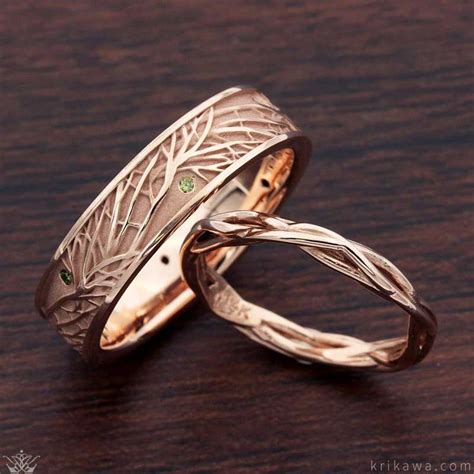 Two Gold Wedding Bands With Green Stones On Them Sitting On A Wooden