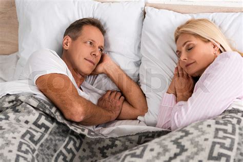man looking at sleeping wife in bed stock image colourbox