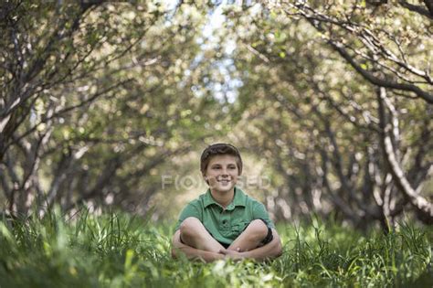 Boy Sitting With Crossed Legs In Woodland Tunnel Of Overarching Tree
