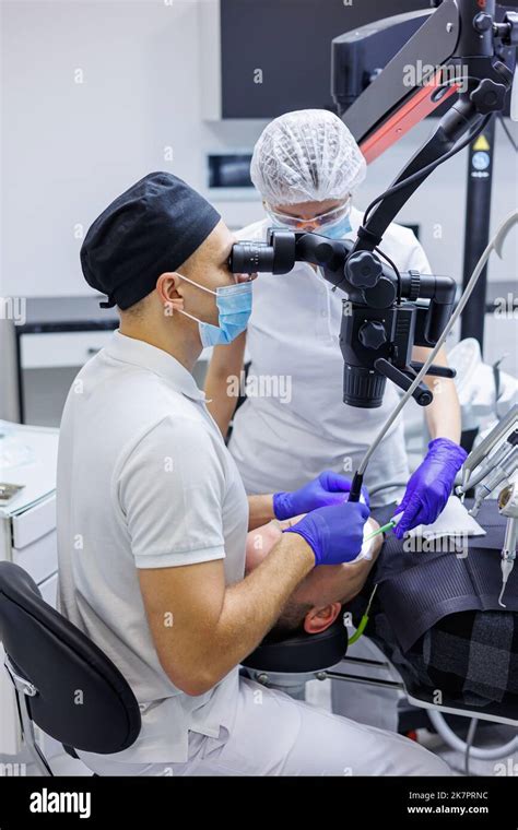 A Dentist And An Assistant Treat A Patients Teeth Using A Microscope