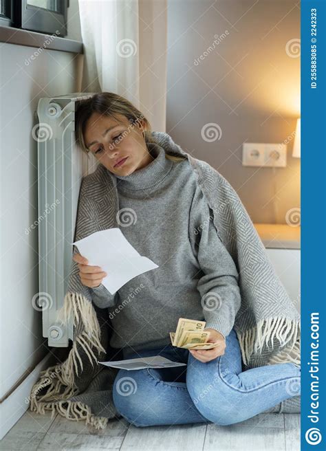 Young Woman Covered With Warm Blanket Sits On Floor Near Radiator Looking At Bills With Upset