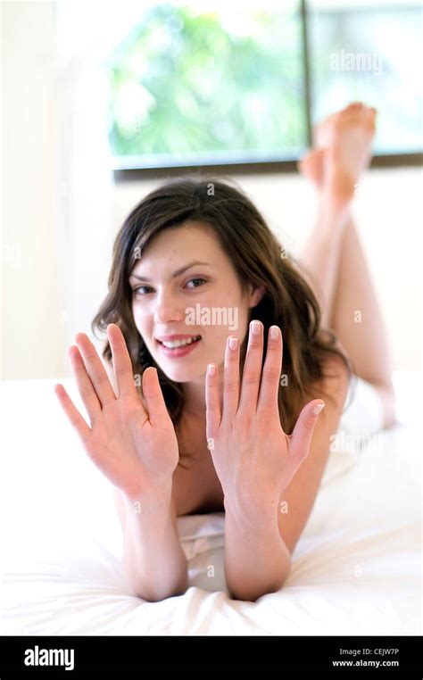 Female With Brunette Hair Laying On Her Front On A Bed Holding Up Her Hands To The Camera Stock