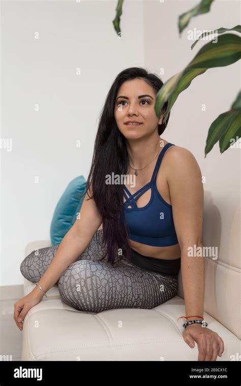 Beautiful Young Woman Doing Stretching Exercises On A White Sofa With Colorful Cushions Inside